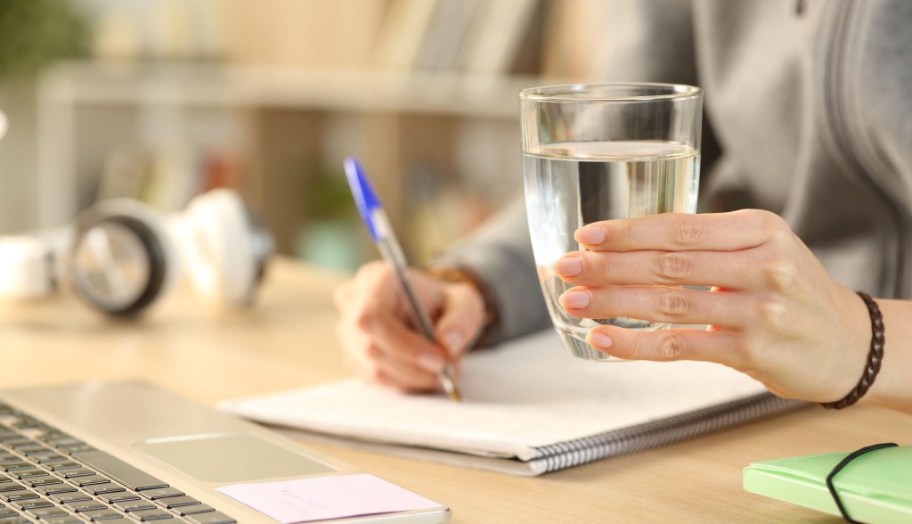 person holding glass of water and taking notes