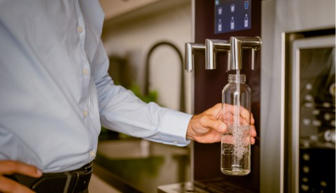 man filling up glass water bottle from water dispenser