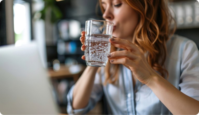 woman drinking sparkling water in front of computer